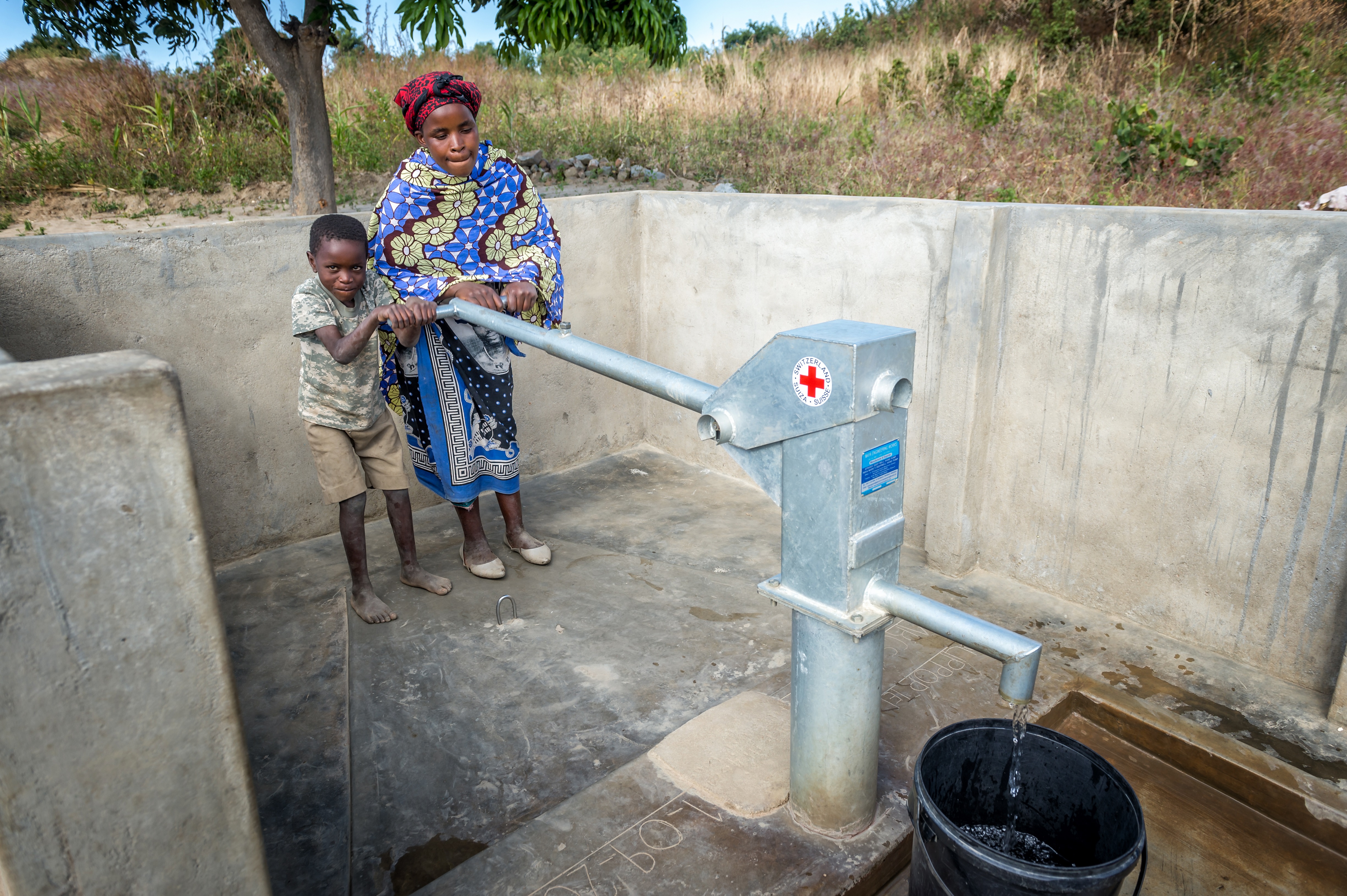 Moles Vuma (54) und ihre Sohn Professor an der Wasserstelle, die das SRK zusammen mit dem Malawischen Roten Kreuz für die Bewohnerinnen und Bewohner von Maganjira gebaut hat. Die Mauer zum Schutz der Wasserstelle wurde von den Dorfbewohnern selber gebaut.